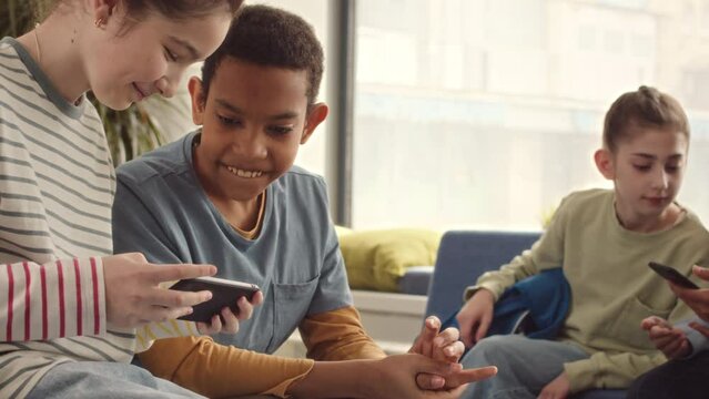 Slowmo of diverse middle school kids playing games on smartphone and chatting during break at school