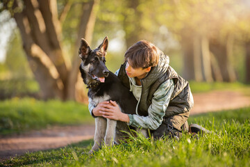 a boy with a dog walk in the park on a sunny spring evening, sit on the grass. Friendship of man and animal, healthy lifestyle.