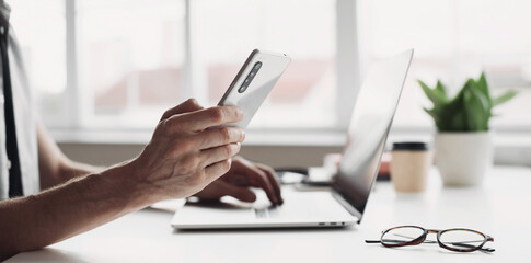 Fototapeta premium Man hands using smart phone and laptop at home closeup, Businessman or student working on computer and texting smartphone at office, Freelance, business, education and technology concept