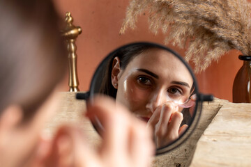 Mirror image of a woman removing patches under the eye on a dressing table 