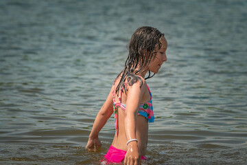 A little girl splashes in a pond during the day.