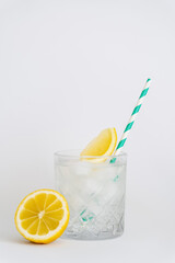 faceted cold glass with ice cubes, paper straw and sliced lemons on white.