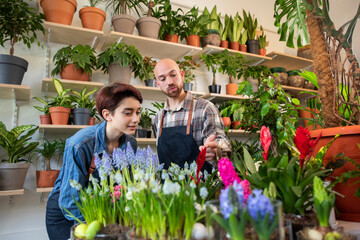 Beautiful woman working as florist in floral store she have a conversation with her colleague sales assistant guy they holding a floral in hands and smiling large