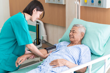 An Asian surgeon in Thailand meets an elderly patient who has undergone surgery to inquire about the condition and check the health of a patient lying on a hospital bed.