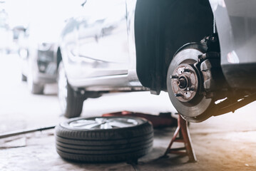 Repairing the breaks of a car after a street crash. Details and focus on metal parts and worn out disc, Close up disc brake without wheels of the vehicle for repair. - obrazy, fototapety, plakaty