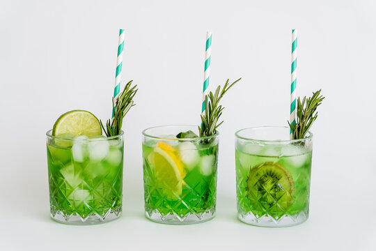 faceted glasses with green cocktail, ice cubes and fruits on white.