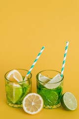 sliced citrus fruits in glasses with sparkling mojito drink and straws on yellow.