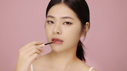 Close up face of beautiful young Asian woman applying lip on her lips on pink background.