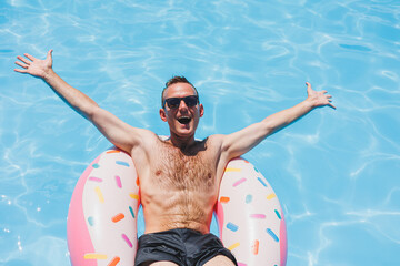 A young man in sunglasses and shorts is relaxing on an inflatable donut in the pool. Summer vacation - Powered by Adobe