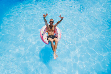 A young man in sunglasses and shorts is relaxing on an inflatable donut in the pool. Summer vacation