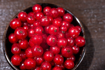 Red currants in a black bowl on a wooden background. Harvest of ripe summer berries