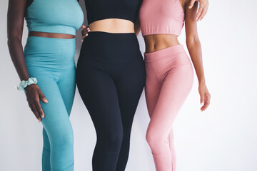 Cropped diverse female in trendy tracksuits posing during sportive photo session in gym aerobic studio, unrecognizable multicultural yoga partners enjoying collaborative workout teamwork indoors