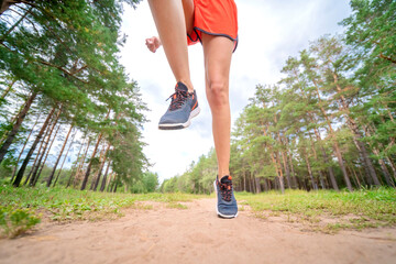 Closeup of athlete's feet running at the park. Fitness woman jogging outdoors. Exercising on forest...