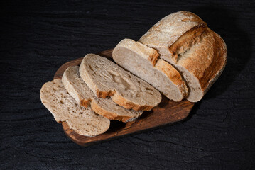 Sliced yeast grain bread with oats on dark concrete background