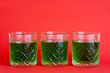 green alcohol drink in three faceted glasses with water drops on red.