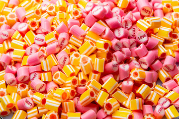 Bunch of pink with inscription Love and yellow striped caramel candies. Mix of colorful sweetmeat lollipops close up. Sweet sugar dessert. Candy Shop. Background for holiday or children's birthday.