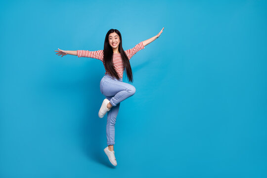 Full length photo of pretty charming lady dressed red shirt jumping high arms sides empty space isolated blue color background