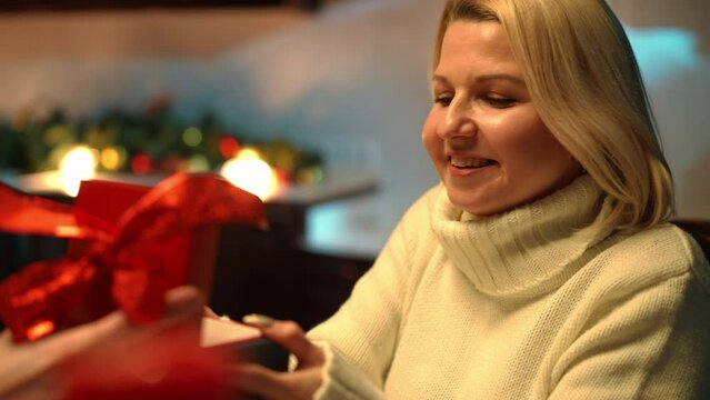 Excited surprised woman receiving Valentine's gift box from unrecognizable man indoors. Portrait of smiling loving happy Caucasian girlfriend wife enjoying holiday. Romance concept