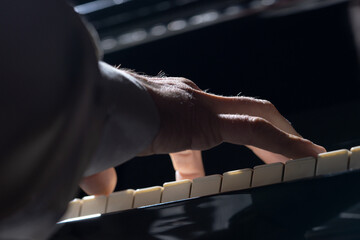 Bottom view of male hands touching black and white piano keys. Musician plays a melody with his fingers on a musical instrument in the dark. Musical artist. Screensaver for a music school. Close up. © kinomaster