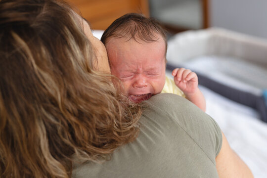 Mid adult caucasian mother pampering newborn crying baby in bedroom at home, copy space