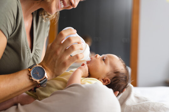 Caucasian mid adult mother feeding milk to cute newborn baby with bottle at home, copy space