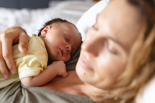 Caucasian mid adult mother with cute sleeping newborn baby resting in bedroom at home