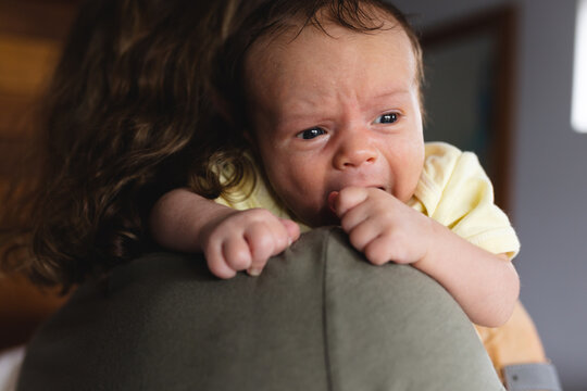 Cute crying newborn baby carried by caring mid adult caucasian mother at home