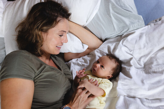 Smiling mid adult caucasian mother lying with cute newborn baby on bed at home, copy space