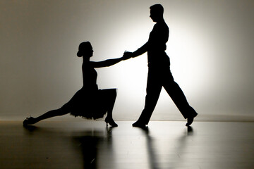 Black silhouettes of pair of ballroom dancers performing elements of Argentine tango. Man and woman...