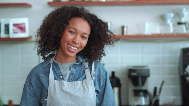 Cheerful woman barista looking at the camera while standing in cafe
