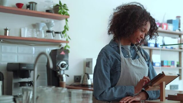 Happy woman barista counting at the checkout while standing in cafe