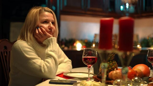 Sad bored woman sitting at romantic dinner table checking phone drinking wine thinking. Portrait of upset Caucasian girlfriend wife waiting for partner on Valentine's Day. Loneliness and lifestyle