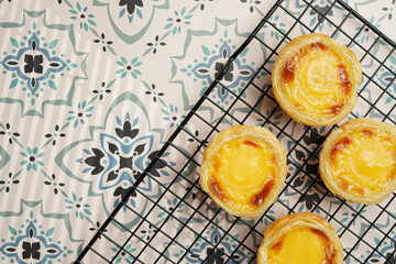 Traditional portuguese vanilla pudding puff pastry pastel de nata on black oven rack on blue tiles...