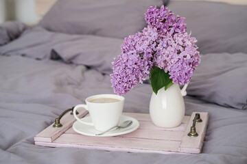 Breakfast in bed. Tray with coffee and a bouquet of lilacs on the bed in the bedroom