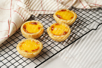 Traditional portuguese vanilla pudding puff pastry pastel de nata on black oven rack on marble background with checkered kitchen towel