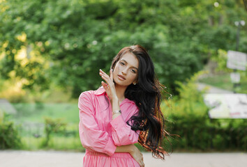 Closeup portrait of a brunette with wavy hair, wearing a pink dress in the park