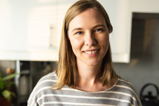Close-up portrait of caucasian mid adult woman smiling in domestic kitchen at home, copy space
