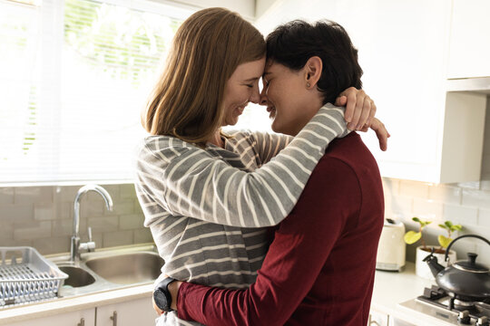 Side view of loving caucasian lesbian couple with eyes closed embracing and romancing in kitchen