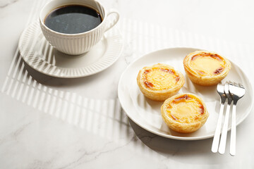 Traditional portuguese vanilla pudding puff pastry pastel de nata on black oven rack on white plate with a cup of coffee in white porcelain