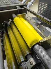 Yellow ink in the paint system compartment of a modern flexographic printing press in a print shop. Yellow paint in the ink feeder on the printing cylinder. Selective focus