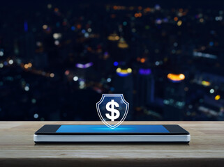 Dollar with shield flat icon on modern smart mobile phone screen on wooden table over blur colorful night light city tower and skyscraper, Business money insurance and protection online concept
