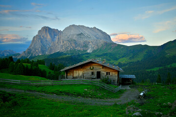 Fototapeta na wymiar Eine Urige und Alte Berghütte aus Holz auf der Seiser Alm und im Hintergrund sieht man den Mächtigen Lang- und Plattkofel in der Dämmerung.