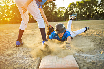Group of two baseball players play together on the playground. On of them slide on the goal