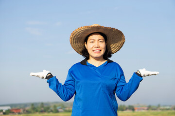 Happy Asian woman farmer. wears hat, blue shirt, smiles, feels excited, make gesture to present...