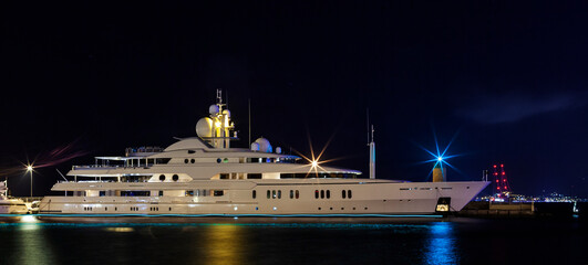 Obraz premium Yacht illuminated by night lights of a port