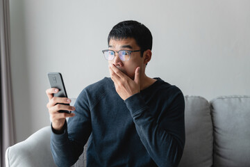 Portrait of excited asian man looking at mobile phone, man receiving good news using smartphone at home.