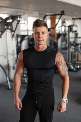 Fototapeta na wymiar Fashionable handsome athletic trainer guy with a muscular body in black sportswear in the gym