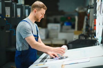 Man worker measuring printing color with spectrometer on the operating desk of the printing plant