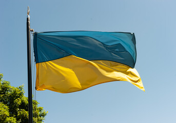 The blue-yellow flag of Ukraine flutters in the wind against the background of the blue sky.