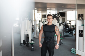 Fototapeta na wymiar Sports handsome bodybuilder trainer guy with a muscular healthy body with a tattoo in a black t-shirt mock up with sportswear in the gym